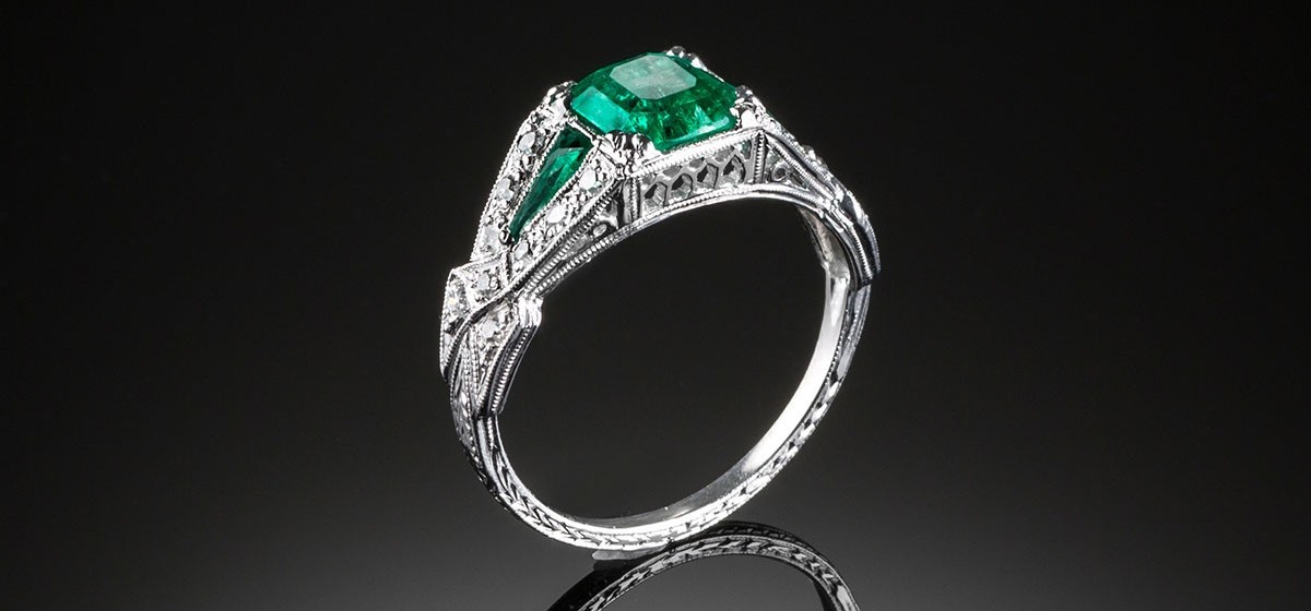 An Art Deco diamond and emerald ring with emerald shoulders