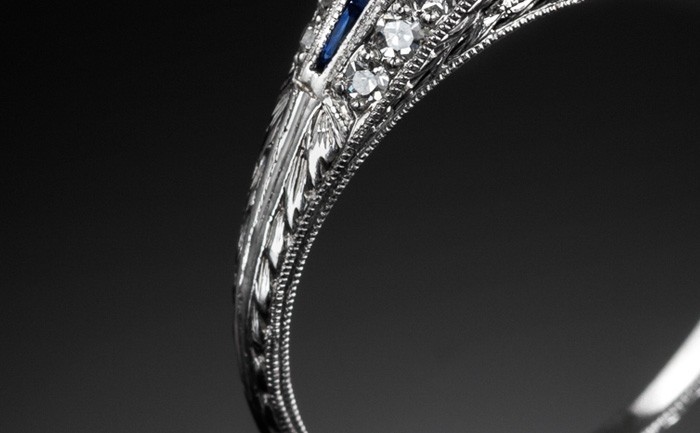 Detail of An Art Deco solitaire diamond ring with diamond and calibre cut sapphire shoulders