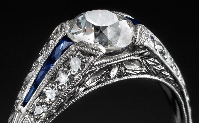 Detail of An Art Deco solitaire diamond ring with diamond and calibre cut sapphire shoulders
